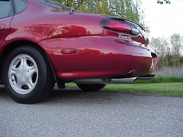 Red sedan's rear quarter panel, wheel, and dual exhaust tips. Badge says Taurus SE