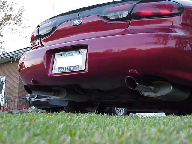 Ground-level rear view of a dark red Ford sedan with dual polished exhaust tips