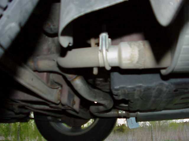 Underside of car showing exhaust pipe with clamp and hanger, crossmember, and rear tire
