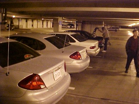 2001 Ford Taurus - A silver 2001 Ford Taurus is parked in a garage, with other vehicles and people in the background.