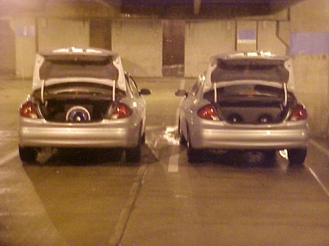 2001 Ford Taurus - Two silver sedans with open trunks are parked in a dimly lit, possibly underground, parking area.