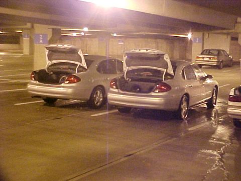 2001 Ford Taurus - Two silver Ford Taurus sedans, likely from the early 2000s, are parked with their trunks open in a dimly lit parking garage.