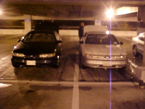 2001 Ford Taurus - Two sedans are parked side-by-side in a dimly lit parking garage, with a person visible between them.