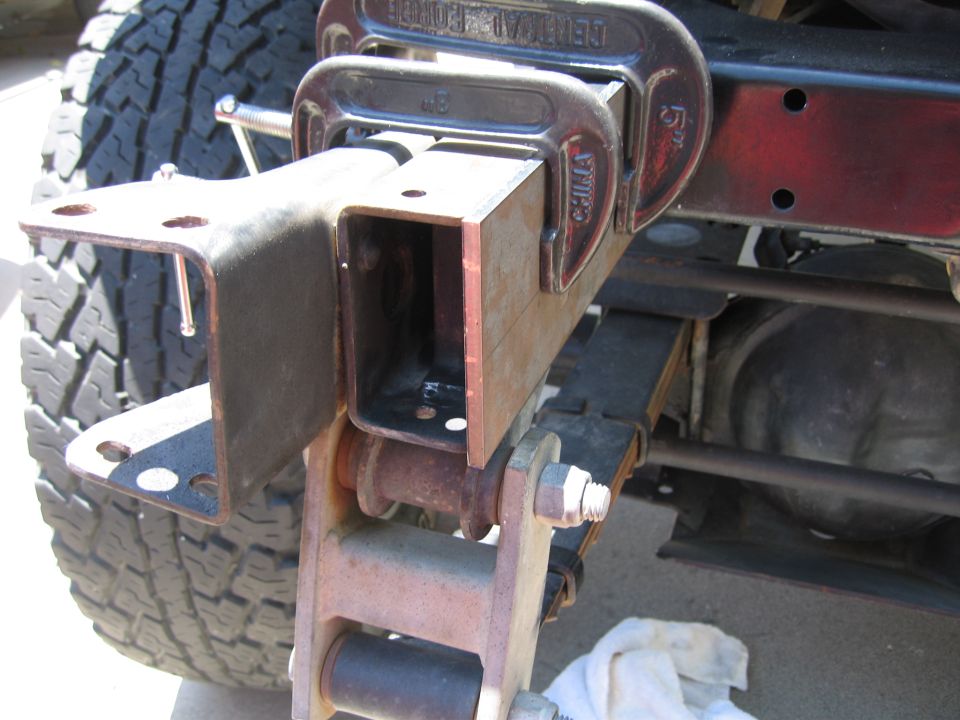 C-clamps holding a metal bracket onto a vehicle's frame near leaf springs and a tire