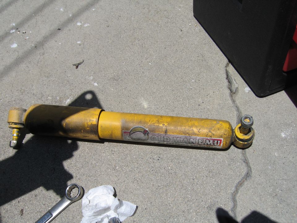Used yellow Old Man Emu shock absorber lying on concrete beside a wrench