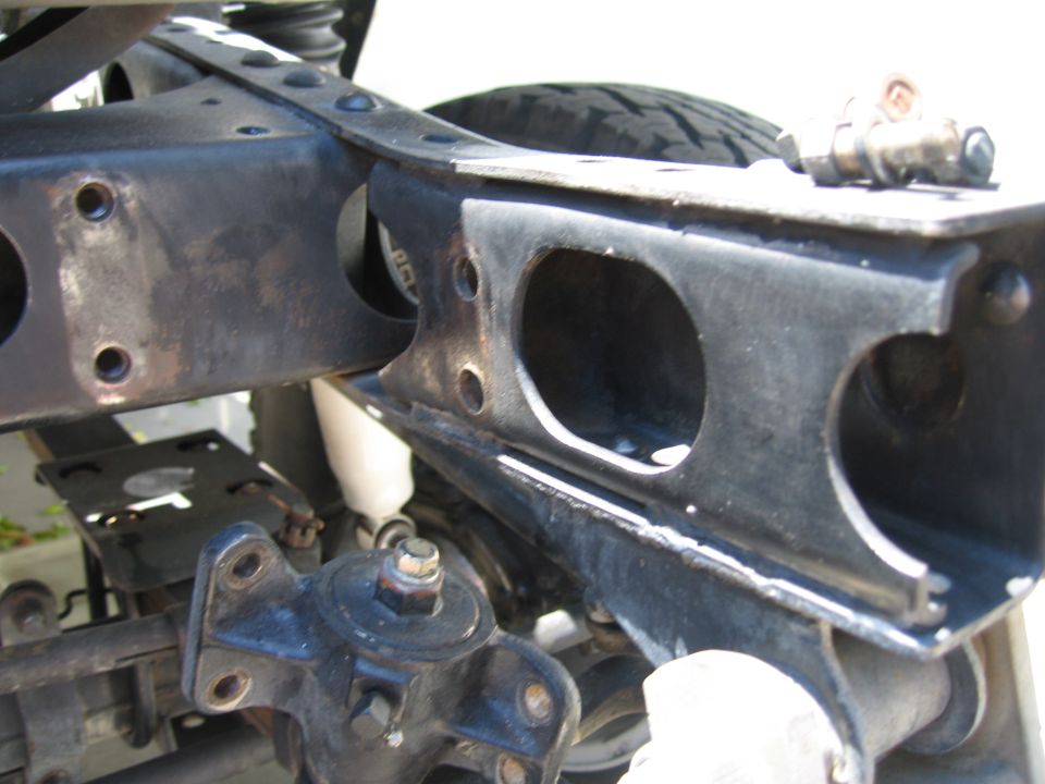 Close-up of black 4x4 rear frame rails, crossmember and shackle mount with white shock