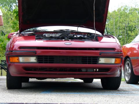 1991 Ford Probe - Front view of a maroon/dark red Ford coupe with its hood raised, showing the engine bay and revealing pop-up headlights, amber turn signals…
