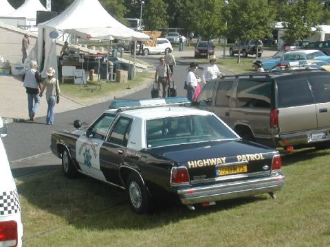 1991 Ford Crown Victoria - A black and white Ford Crown Victoria police car is parked on grass, with a highway patrol decal on the door and text on the trunk.