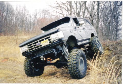 1988 Ford Bronco - Modified Ford Bronco navigates an off-road obstacle with its front wheels angled upwards.