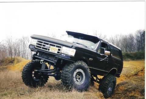 1988 Ford Bronco - This lifted 1988 Ford Bronco is shown off-roading on a dirt hill with large tires and suspension modifications.
