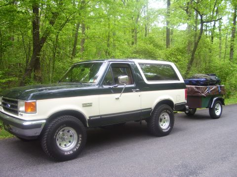 1991 Ford Bronco - Two-tone 1991 Ford Bronco is seen from the side, towing a trailer packed with luggage.