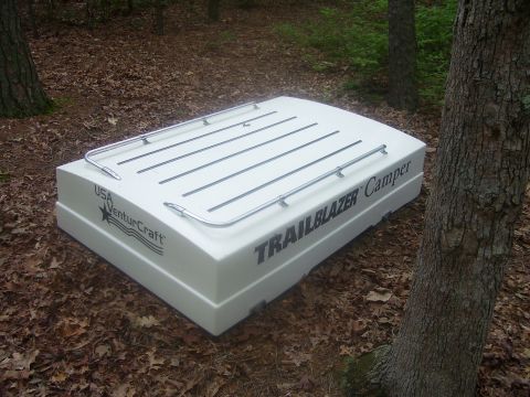1991 Ford Bronco - White fiberglass VenturCraft "Trailblazer Camper" pop-up trailer shell sitting closed on leaf litter in the woods, viewed from a high three…