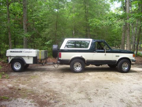 1991 Ford Bronco - Full side profile of a dark green and cream two-tone full-size Ford Bronco with a white removable hardtop, chrome-style wagon wheels and al…