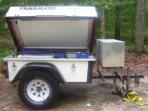 1991 Ford Bronco - A small white off-road utility trailer branded 'TRAILBLAZER Camper' with its lid opened to reveal a slide-out kitchen/galley setup, mounted…