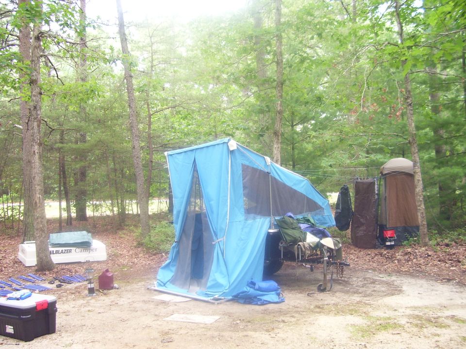 Blue canvas tent trailer camper set up at wooded campsite with Trailblazer Camper lid leaning nearby