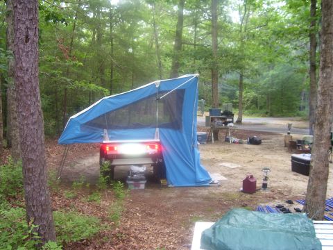 1991 Ford Bronco - Rear view of a vehicle set up as a camping platform with a blue tent/awning extending from its open tailgate, brake or work light illuminat…