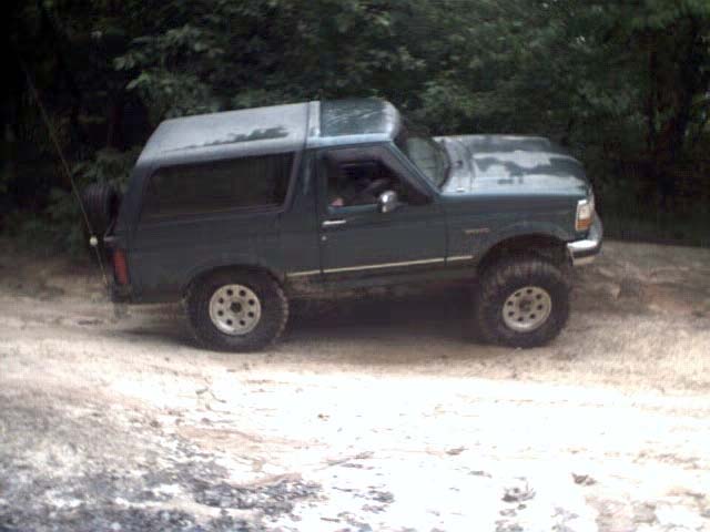 Green 1996 Ford Bronco parked on a dirt road with trees in the background