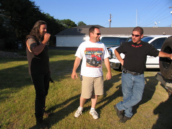 Three men on a lawn at a Bronco event, one in a lifted-Bronco graphic T-shirt