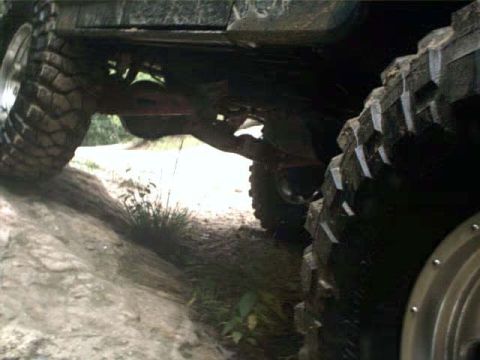 1996 Ford Bronco - The underside and aggressive tires of an off-road vehicle are visible as it navigates a rocky path.