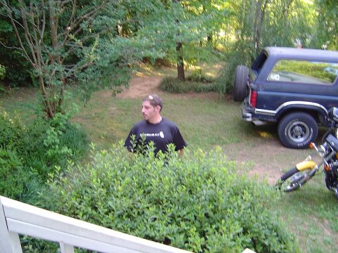 1986 Ford Bronco - A 1986 Ford Bronco is parked in a grassy area next to a motorcycle, with a man standing behind some bushes.
