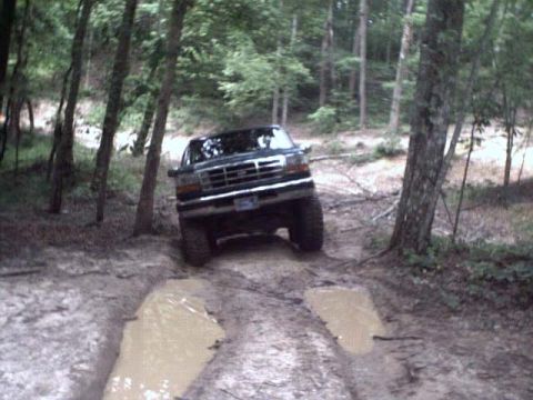 1996 Ford Bronco - This SUV navigates a challenging muddy path in a wooded area.
