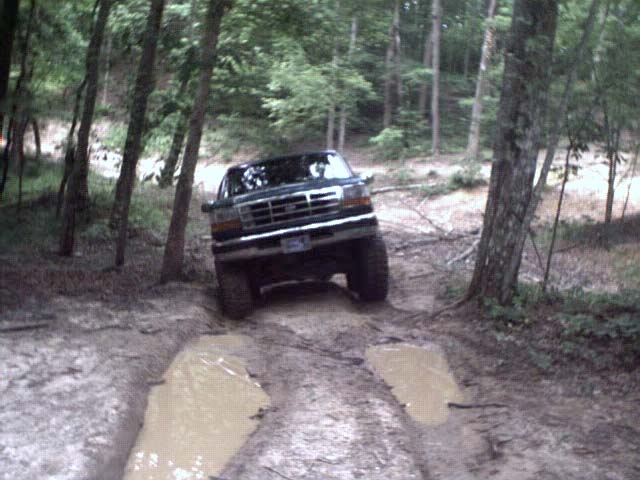 Dark SUV with large tires driving through a muddy trail in a forest