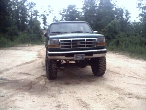 1996 Ford Bronco - A dark green 1996 Ford Bronco is parked on a dirt road, surrounded by trees.