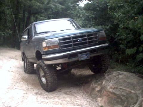 1996 Ford Bronco - A dark green Ford Bronco navigates a rocky trail, its lifted suspension evident as it goes over an obstacle.