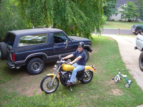 1986 Ford Bronco - A man poses on a yellow motorcycle next to a dark blue 1986 Ford Bronco.
