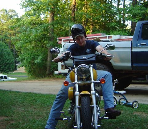 1986 Ford Bronco - Man on a yellow motorcycle with a blue pickup truck in the background.