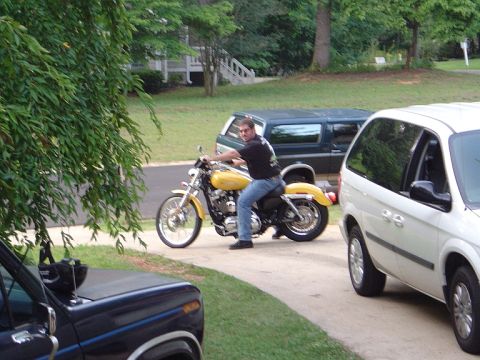 1986 Ford Bronco - A man sits on a yellow motorcycle in a driveway, with other vehicles visible in the background.
