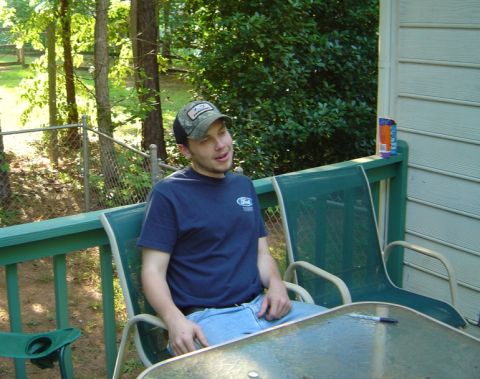 1986 Ford Bronco - A man wearing a Ford t-shirt sits on a deck, with trees and a fence visible behind him.