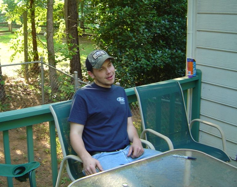 Man in Ford t-shirt sitting on a deck with trees in background