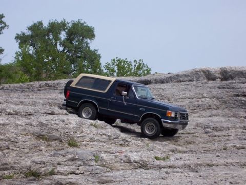 1991 Ford Bronco - A dark blue 1991 Ford Bronco navigates a rocky landscape under a clear sky.