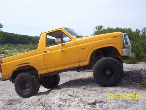 1991 Ford Bronco - This 1991 Ford Bronco is shown off-roading on a rocky surface with trees in the background.