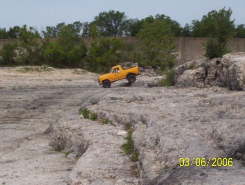 1991 Ford Bronco - A yellow pickup truck navigates a rocky terrain on a sunny day.