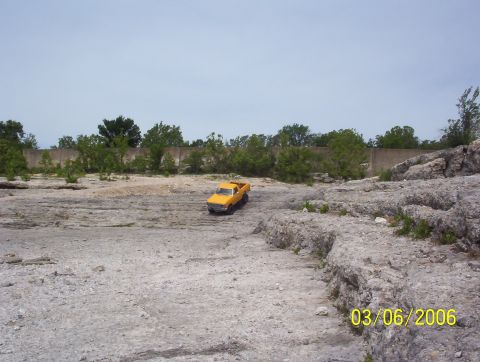 1991 Ford Bronco - A yellow pickup truck is parked in a , outdoor environment with trees and rocks visible.