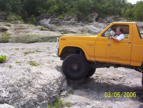 1991 Ford Bronco - A yellow Ford Bronco navigates a rocky terrain near a body of water.