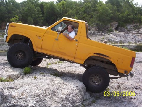 1991 Ford Bronco - A yellow 1991 Ford Bronco navigates a rocky terrain on a sunny day.