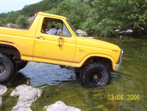 1991 Ford Bronco - A yellow Ford Bronco navigates a rocky stream bed on a sunny day.