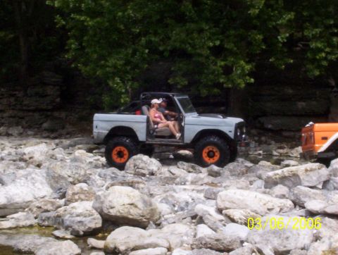 1991 Ford Bronco - Two vehicles, including a 1991 Ford Bronco, are off-roading over rocks near a wooded area.