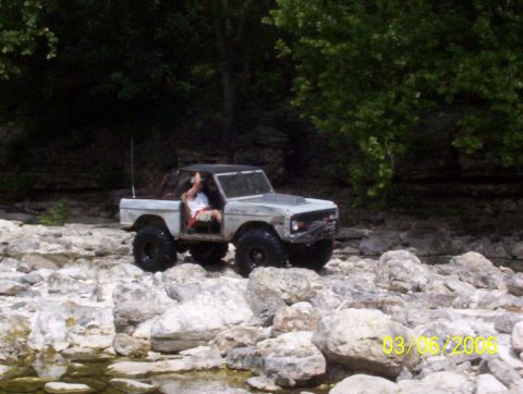1991 Ford Bronco - A classic Ford Bronco navigates a rocky terrain with trees in the background.