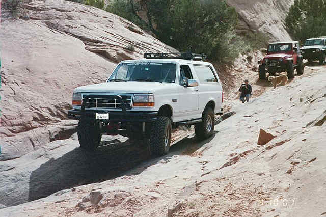Lifted white Ford Bronco on a sandstone trail with Jeeps following behind