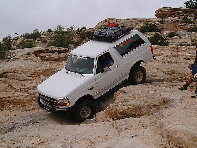 White Ford Bronco with roof rack crawling over slickrock, front wheel dropped into a crevice