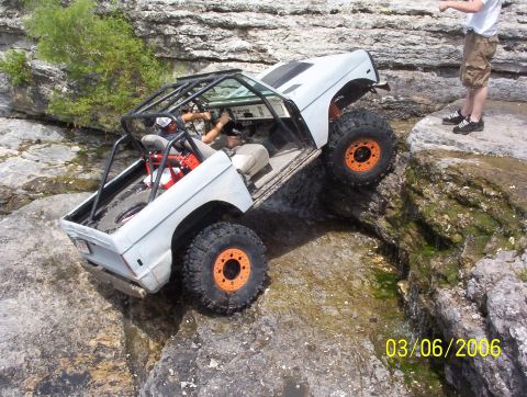 1991 Ford Bronco - A white 1991 Ford Bronco navigates a challenging rocky off-road course with water flowing around it.