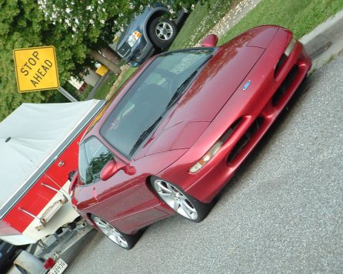 1995 Ford Probe - A red 1995 Ford Probe is parked curbside, with a boat trailer to its left and a blue SUV in the background.
