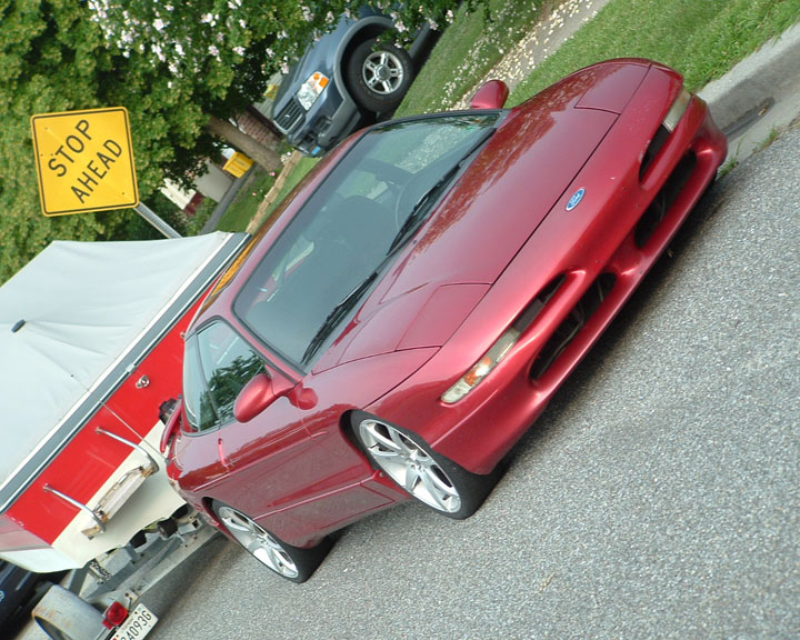 Red 1995 Ford Probe, front 3/4 view, parked next to a boat trailer. Blue SUV visible in background