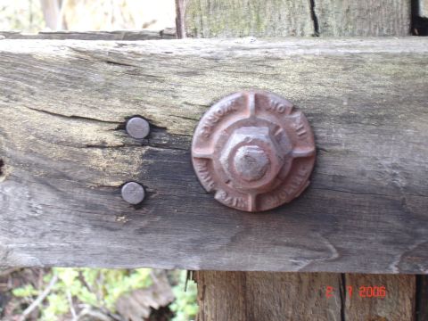 1984 Ford Bronco - Close-up of a rusted bolt with inscribed text, attached to a weathered wooden beam.