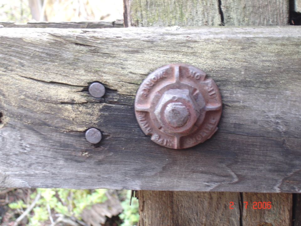 rusted bolt with text on weathered wood beam, two nails nearby