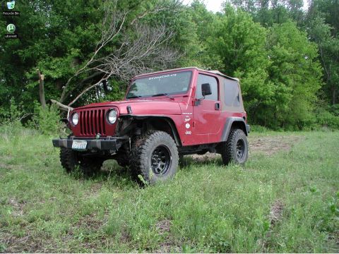 1998 Jeep TJ - A red Jeep Wrangler sits in a field with trees in the background.